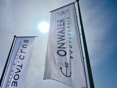 Zwei Beachflags mit den Logos von Onwater Bootsschule und Boat Club vor blauem Himmel am Trainingsstandort Port Calanova