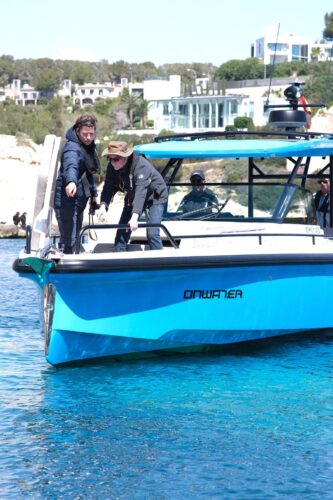 Trainer und Teilnehmer beim Anlegen eines blauen Motorboots mit der Aufschrift Onwater an der Kueste Mallorcas, tuerkisfarbenes Wasser im Hintergrund